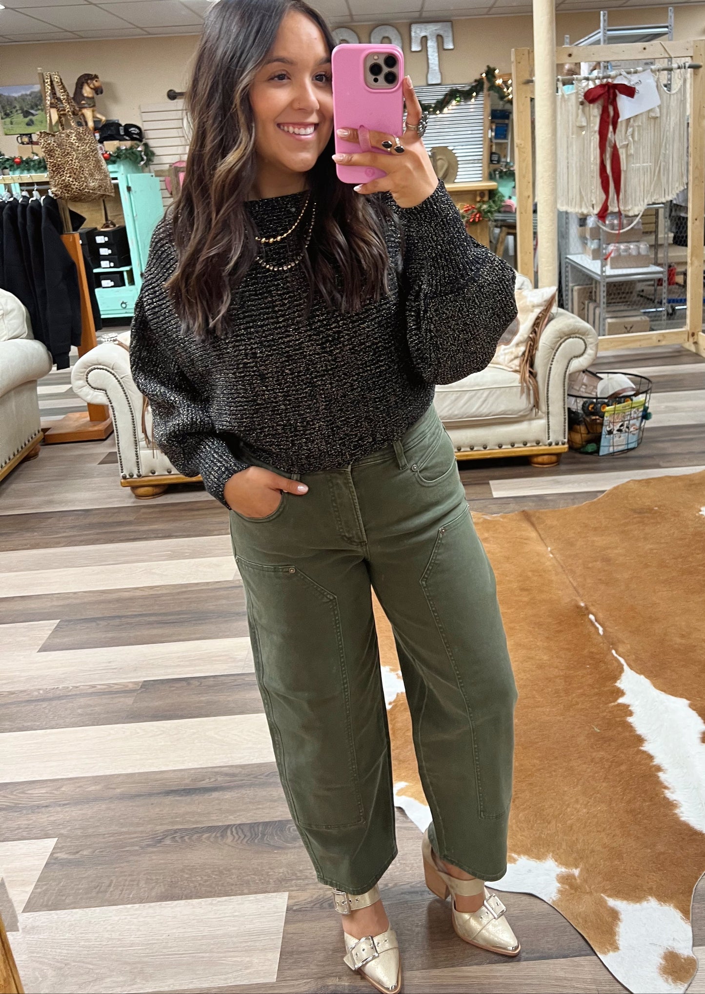 Woman taking a mirror selfie in a store wearing a dark sweater and green pants.