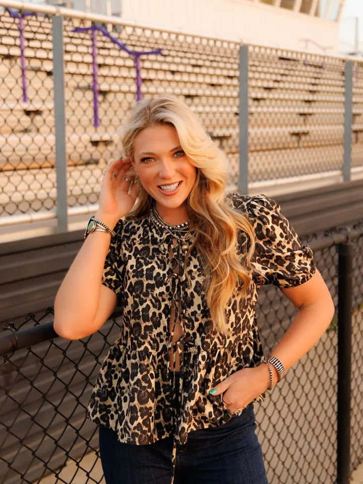 Woman wearing a leopard print top standing in front of bleachers.