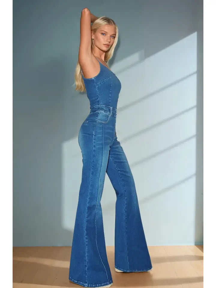 Woman wearing a blue denim jumpsuit standing against a light gray wall.