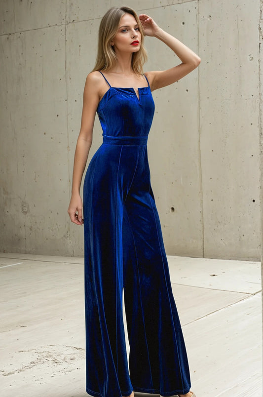 Woman wearing a blue velvet jumpsuit against a concrete wall.
