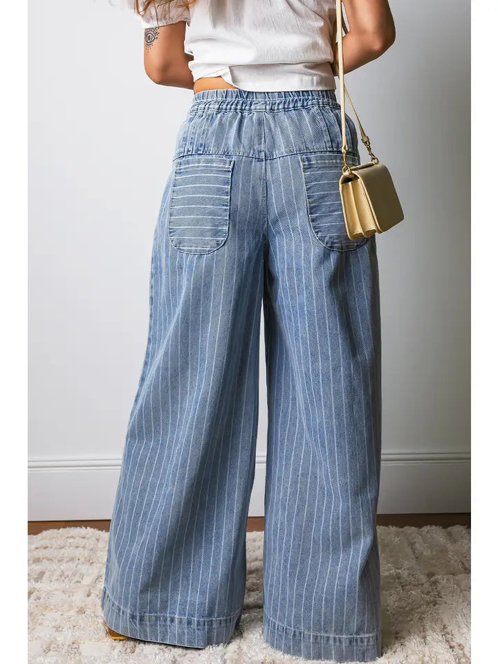 Person wearing blue striped pants with a white shirt and gold handbag on a neutral background