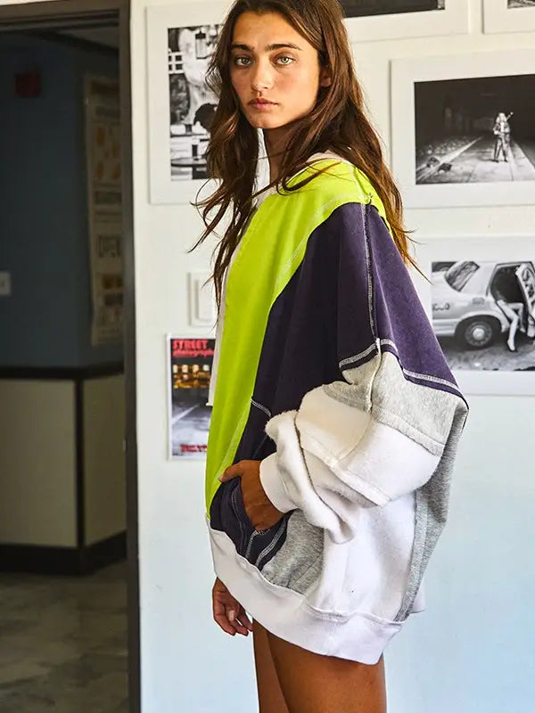 Woman wearing a colorful oversized sweater in an indoor setting with framed pictures on the wall.
