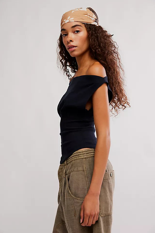 Woman wearing a black top and beige pants with a beige headband against a white background